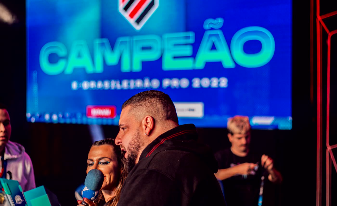 Vitor Abdalla no palco do eBrasileirao Pro 2022, com o telao escrito CAMPEAO atras